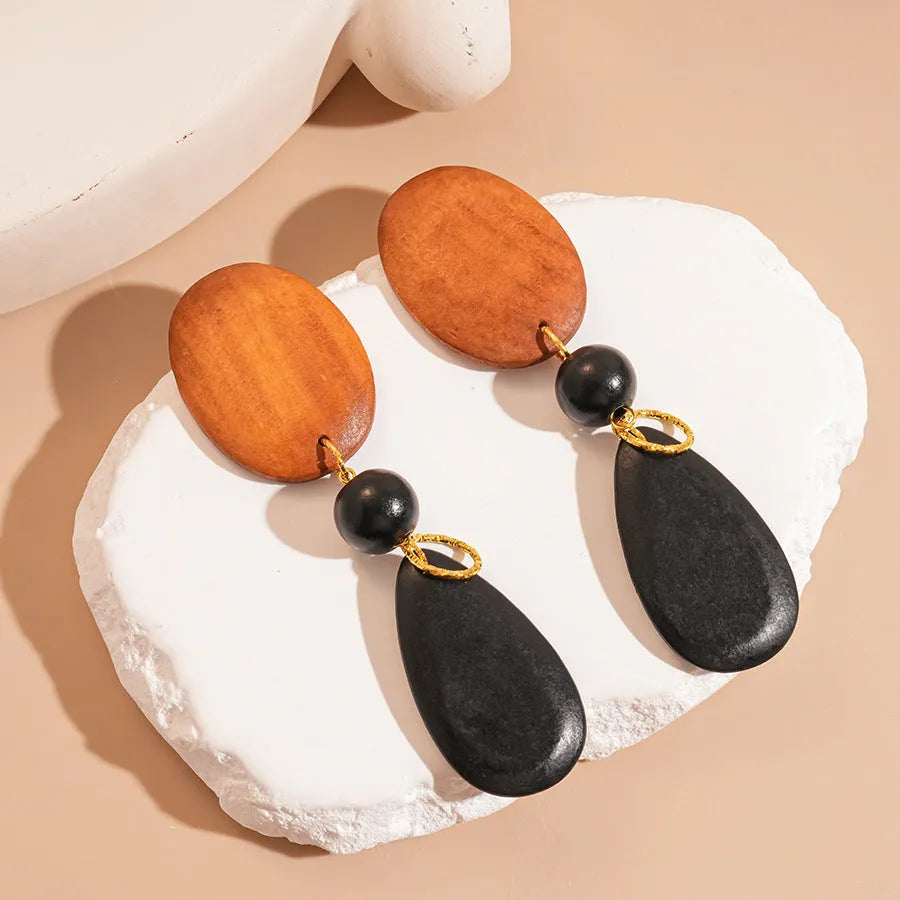 Handmade brown and black wooden ellipse earrings with silver needle fastenings on a white background.