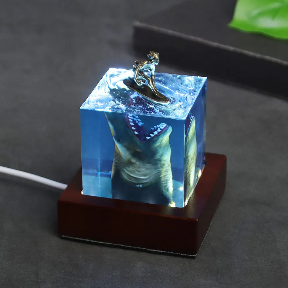 Close-up of a crystal resin shark surfer night light ornament on a dark surface.