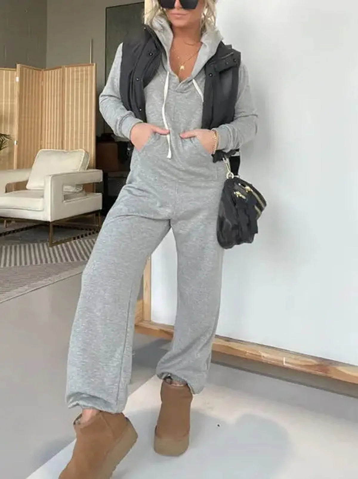 Women's solid colour hooded jumpsuit in black with long sleeves and front pockets on a plain background