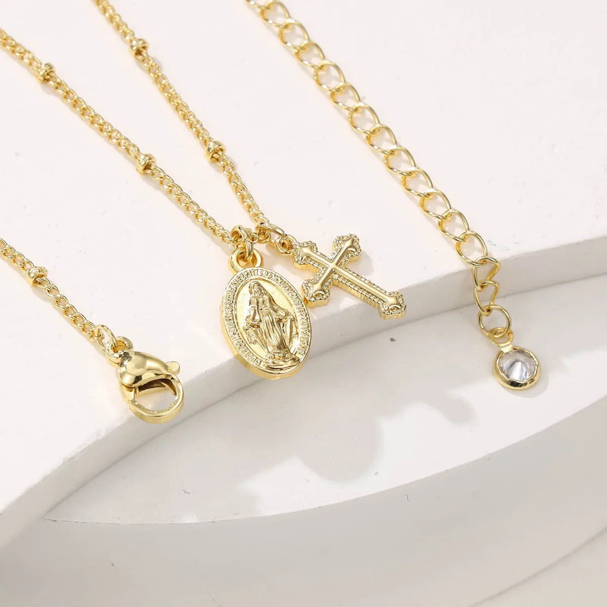 Gold-coloured geometric Virgin Mary and cross pendant necklace on a chain.