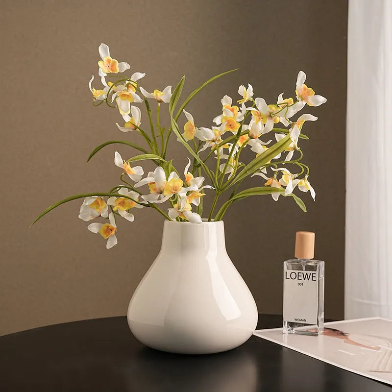Black ceramic round belly vase with white artificial orchids on wooden table