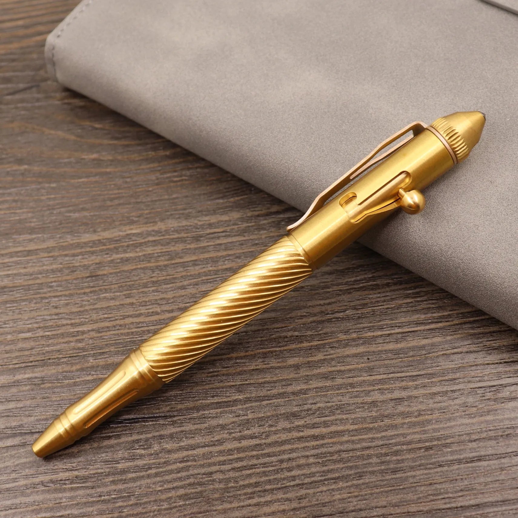 Close-up of a solid brass bolt action tactical pen with a press mechanism on a dark surface.