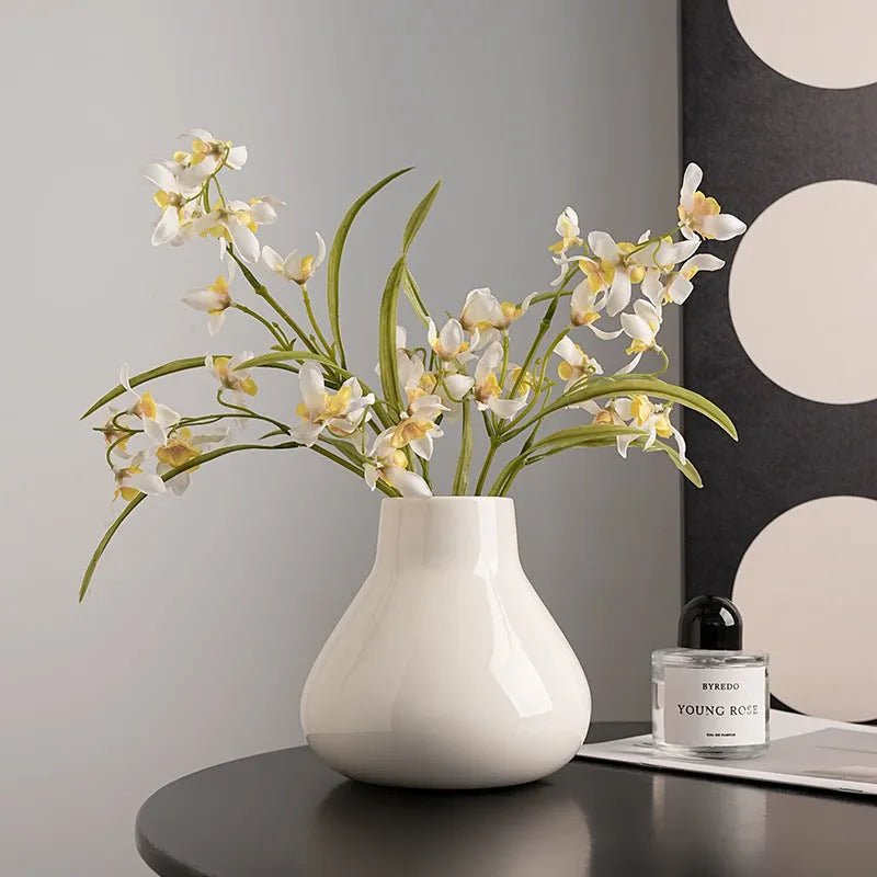 Black ceramic round belly vase with white artificial orchids on wooden table