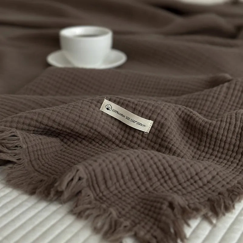 Cotton four-layer gauze blanket with tassel trim in various colours draped over a sofa.
