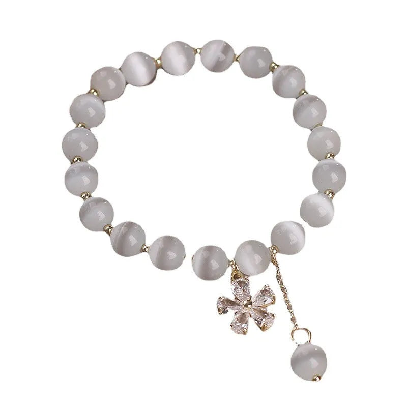 Women's white cat's eye stone bracelet with flower and tassel charms on a single loop.