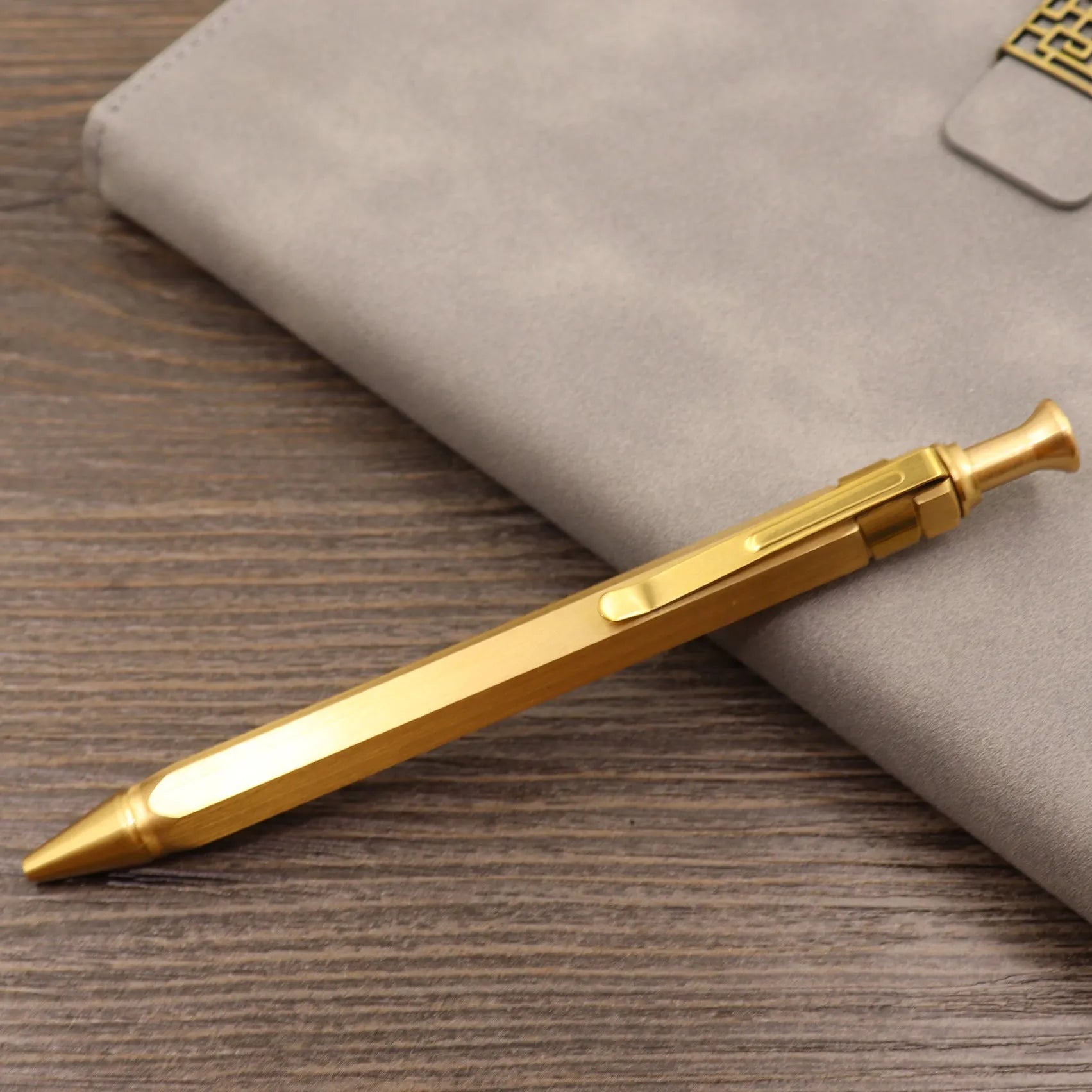 Close-up of a solid brass bolt action tactical pen with a press mechanism on a dark surface.