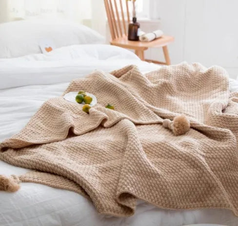 Fringed acrylic knit ball blanket 130x170cm in beige on a sofa