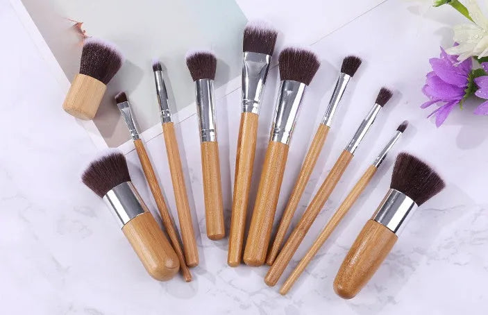 11 bamboo handle makeup brushes arranged on linen bag, including foundation blush and eye shadow brushes
