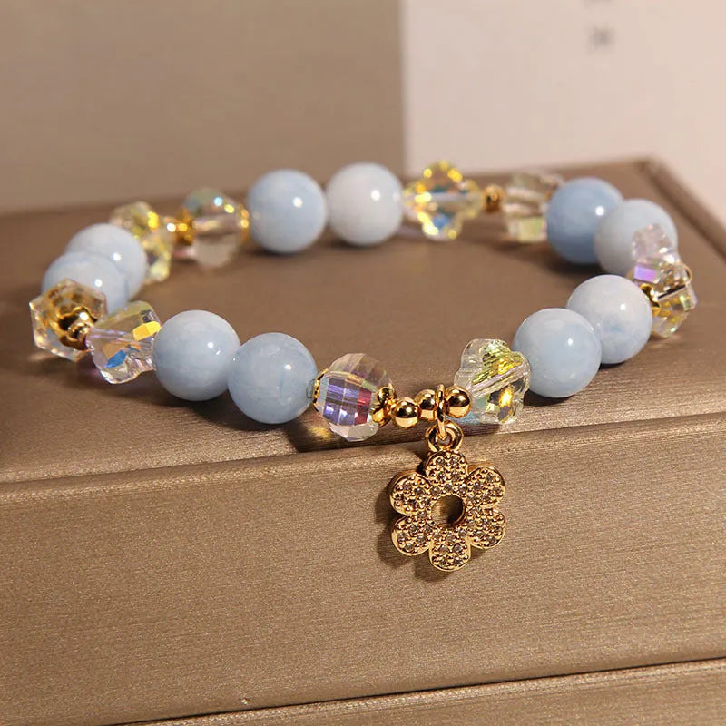 Women's bracelet with aquamarine crystal clover charm and white pearl details on a light background.