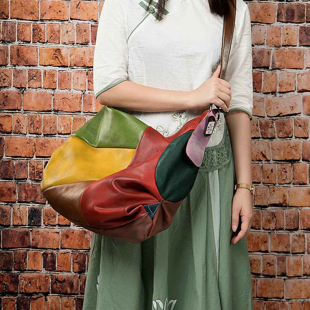 Brown cowhide leather travel bag with stitching details, shown as a crossbody bag holding a laptop.