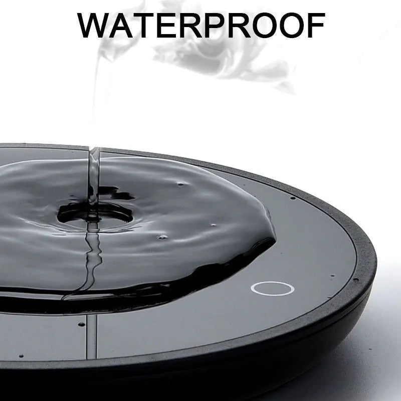 Black circular coffee mug warmer with a tempered glass surface on a desk.