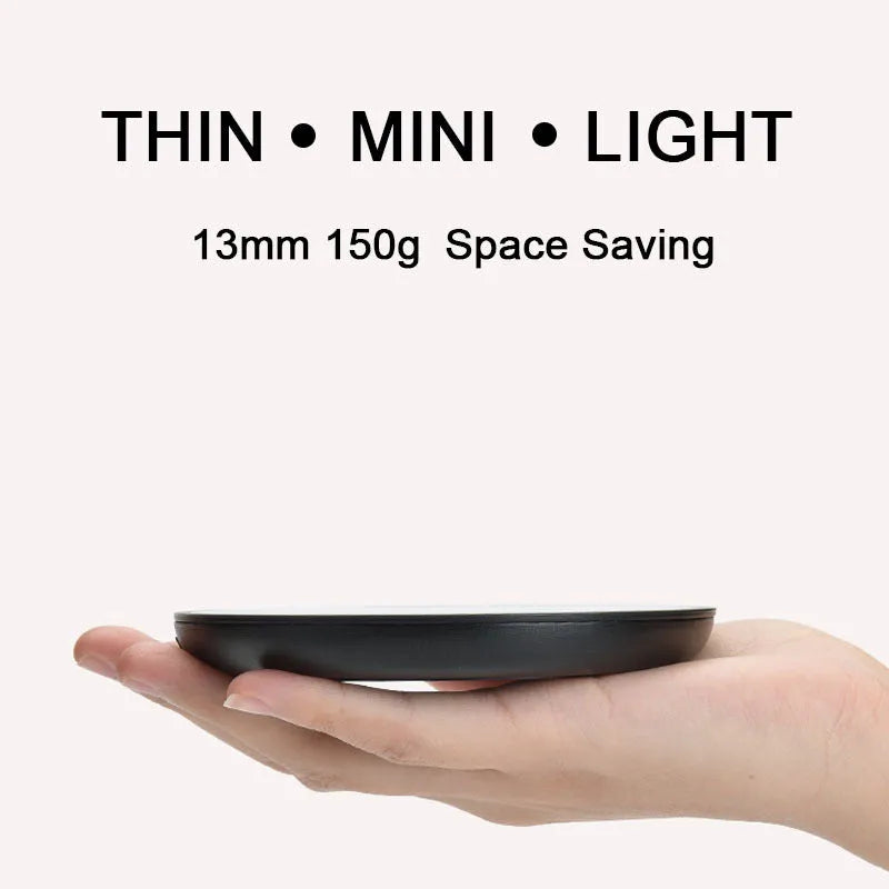 Black circular coffee mug warmer with a tempered glass surface on a desk.