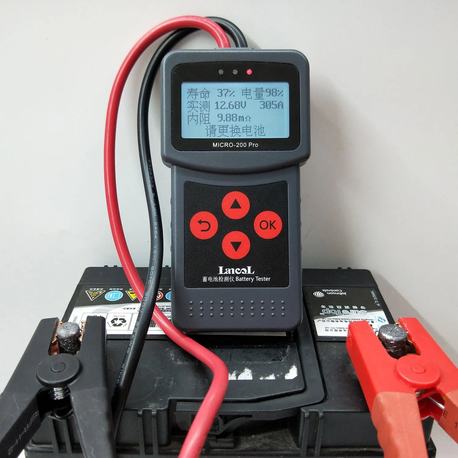 Black car battery tester with digital display measuring internal resistance on a workbench