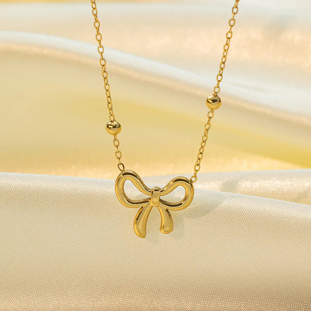 Gold bow necklace with titanium steel cross chain on white background