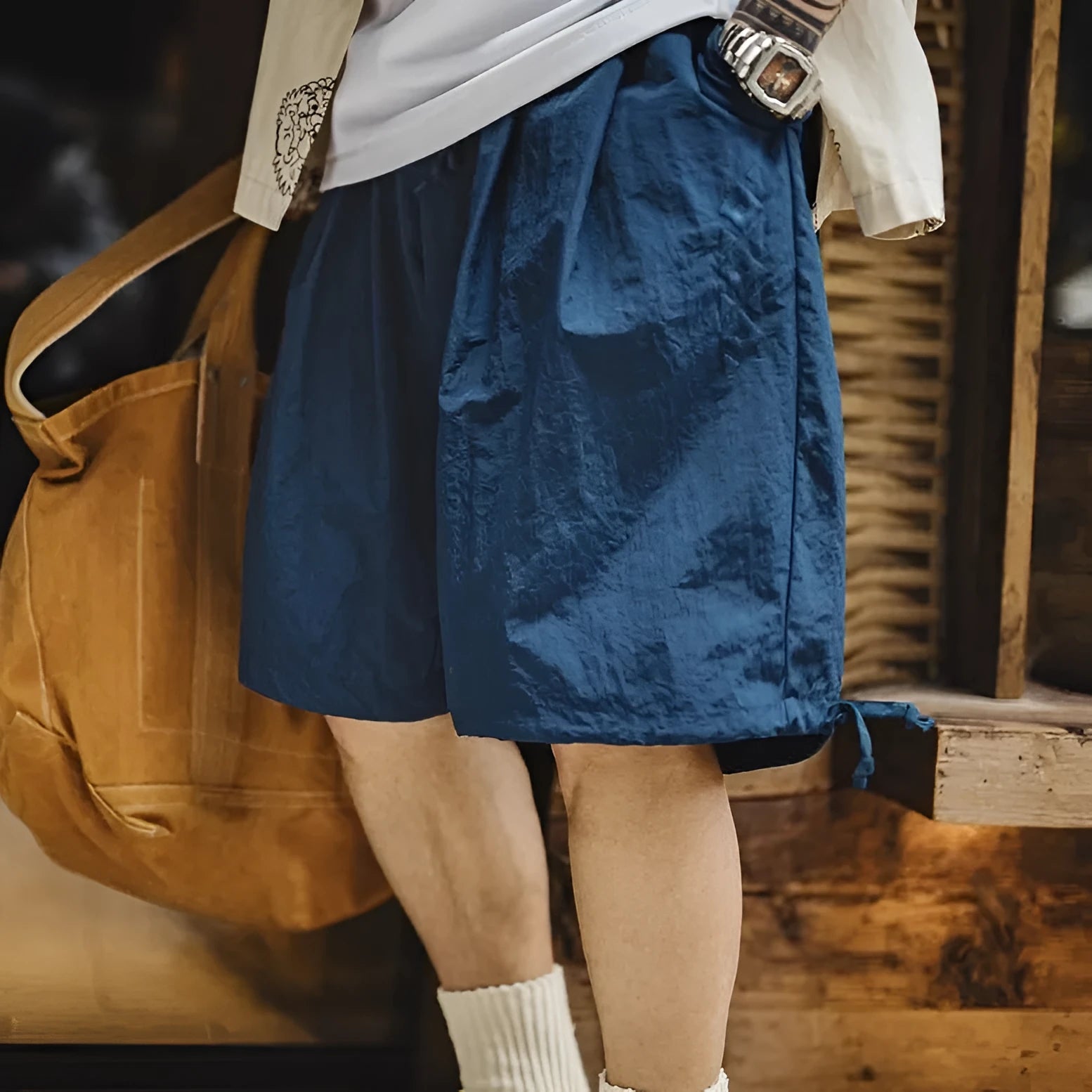 Prussian blue men's loose-fit nylon shorts with embroidery on a summer beach background.