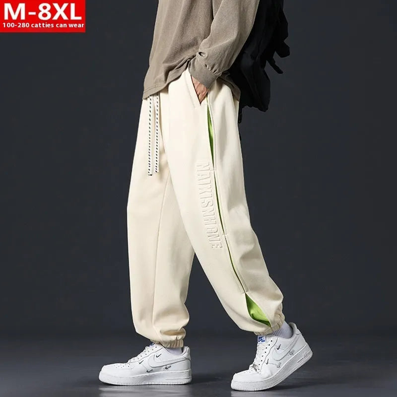 Men's loose black cotton trousers with white collage stitching print and banded ankle cuffs laid flat.