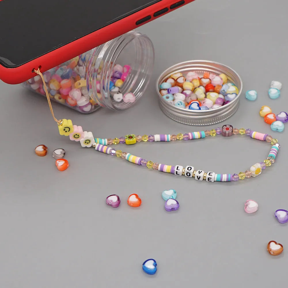 Handmade bohemian smiley soft ceramic beaded phone chain with crystal and acrylic letter beads on a light background