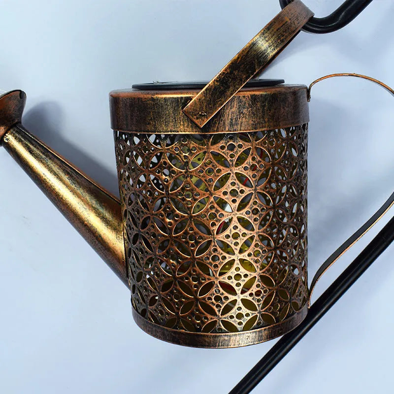 Enchanted watering can solar lamp with warm white star-shaped LED lights in a garden setting