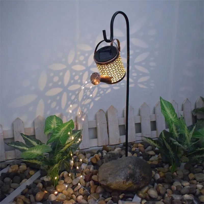 Enchanted watering can solar lamp with warm white star-shaped LED lights in a garden setting