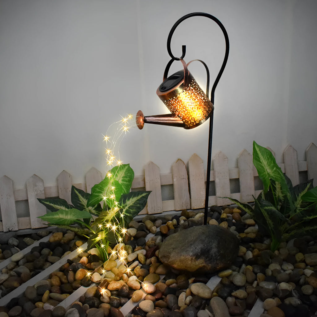 Enchanted watering can solar lamp with warm white star-shaped LED lights in a garden setting