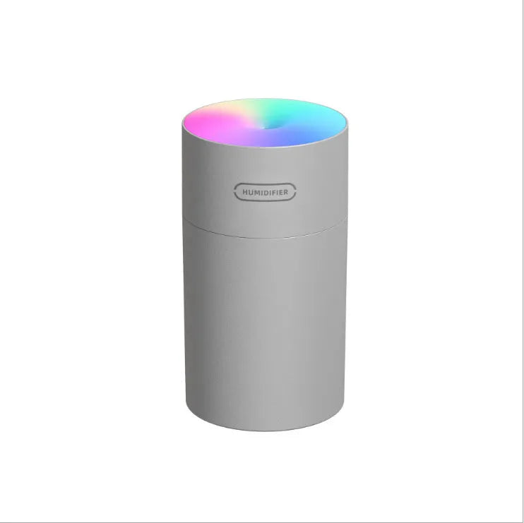 Pink USB desktop humidifier with LED lights and water tank on a wooden desk.