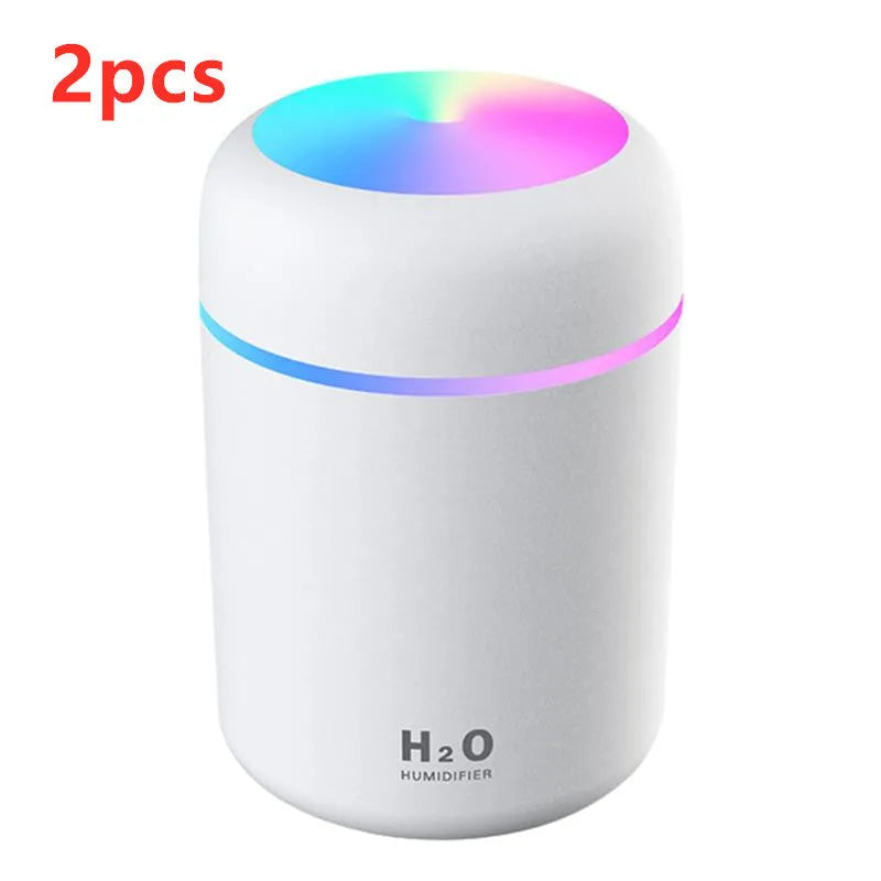 Pink USB desktop humidifier with LED lights and water tank on a wooden desk.