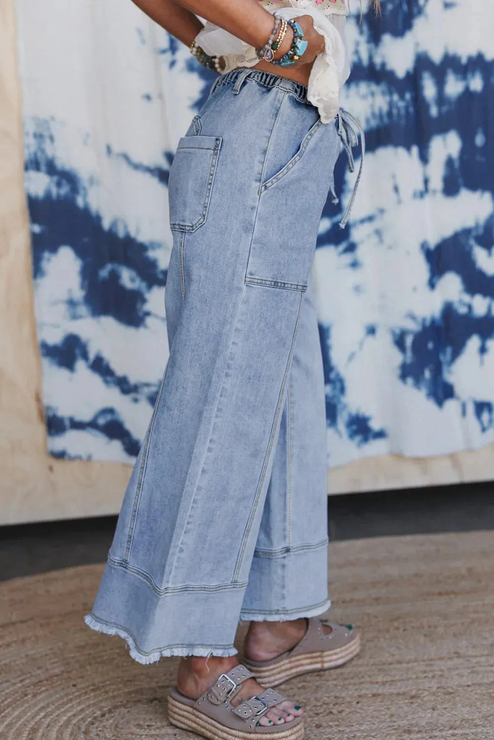 Beau blue wide leg denim trousers with drawstring waist and raw hem detail laid flat
