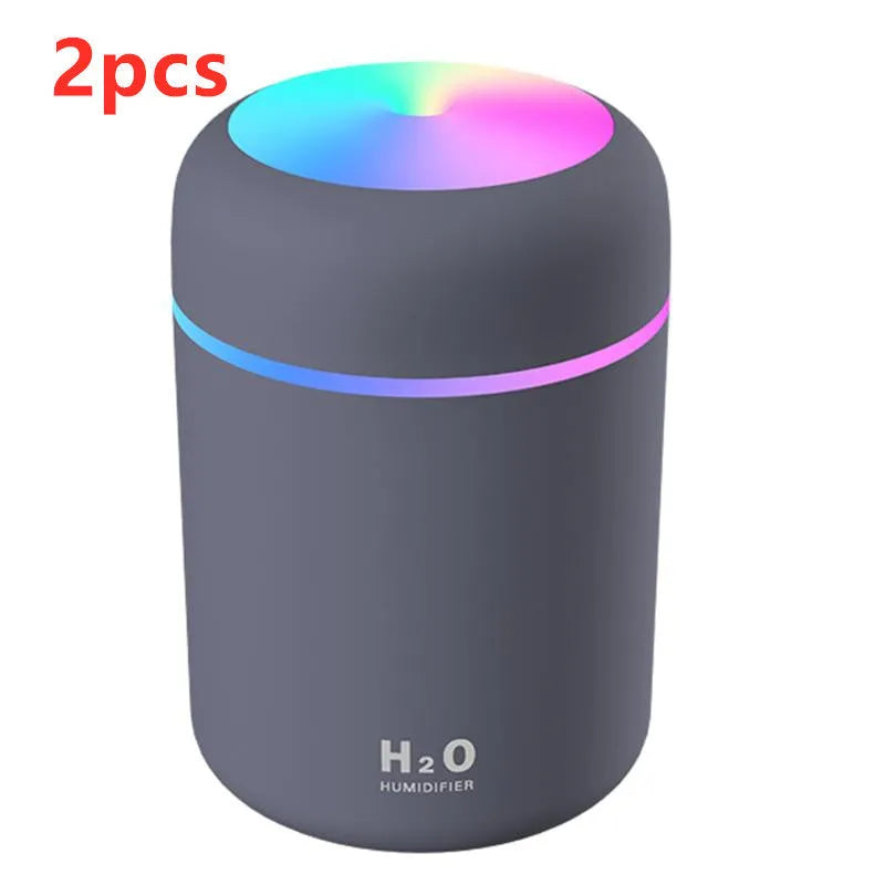 Pink USB desktop humidifier with LED lights and water tank on a wooden desk.