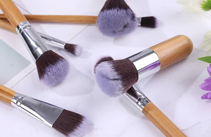 11 bamboo handle makeup brushes arranged on linen bag, including foundation blush and eye shadow brushes