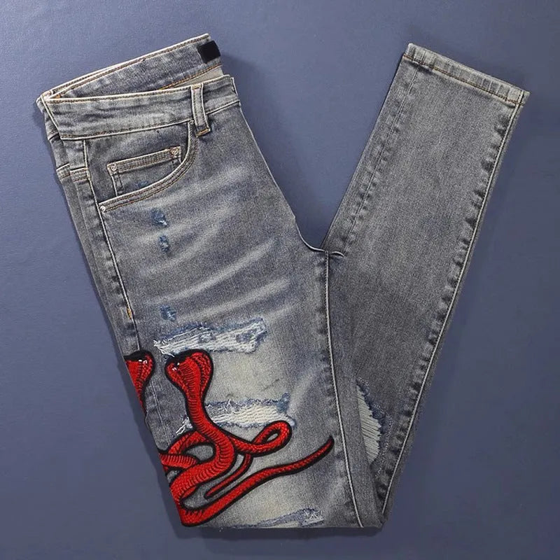 Men's old colour slim fit jeans with worn-out patches, holes, and embroidery on the legs.