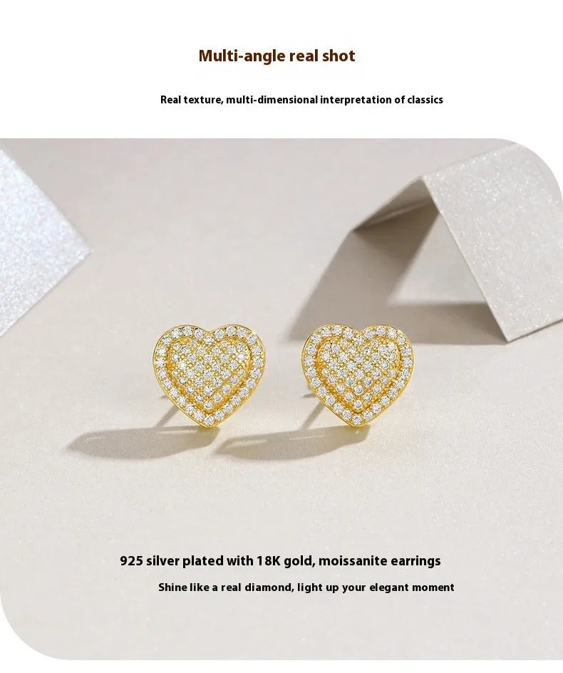 A pair of gold-colour heart-shaped stud earrings with a moissanite stone, on a plain background.