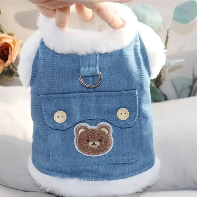Denim dog vest with white wool lining, embroidered teddy bear patches, wooden buttons, and metal D-ring on blue background