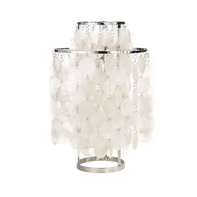 Creative modern shell-shaped table lamp in chrome or gold finish on a bedside table.