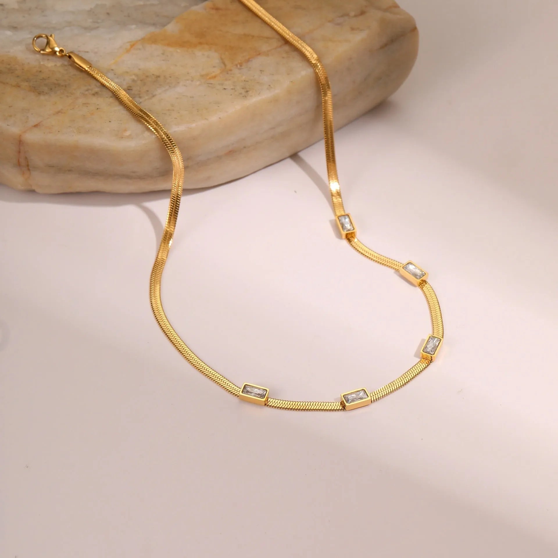 Geometric square zircon pendant on a flat stainless steel snake chain necklace in a gold colour finish.