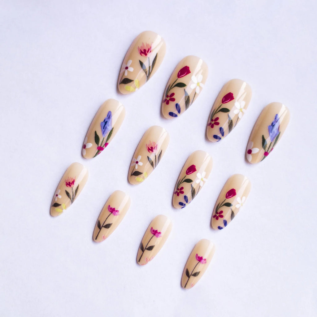 Almond-shaped false nails with detailed 3D pink rose and tulip floral designs on a solid colour base.