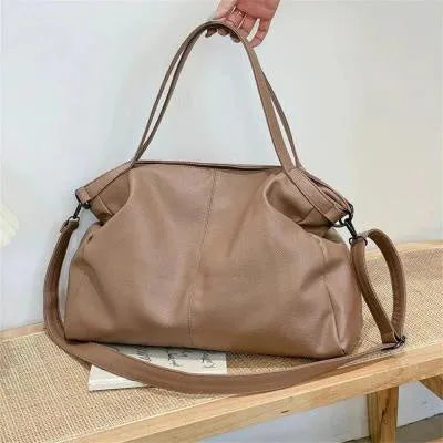 Large soft surface black messenger bag with soft handle and long shoulder strap on a table