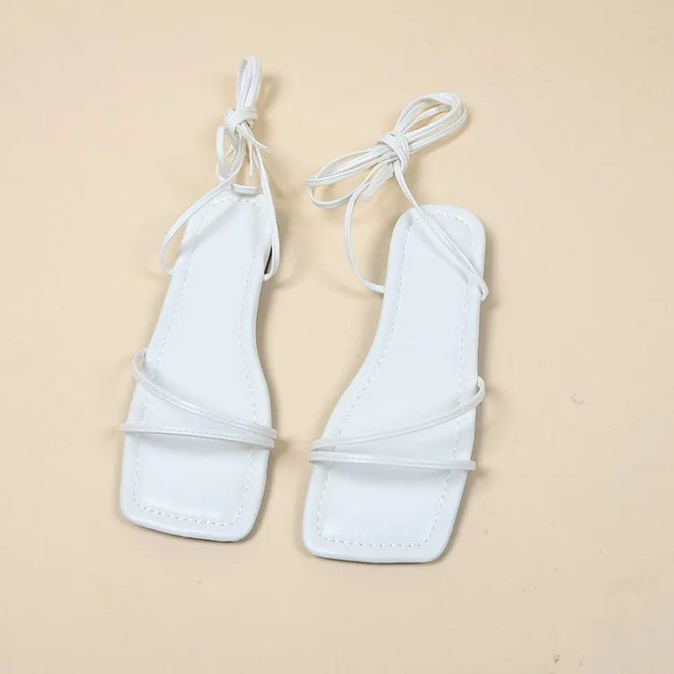 Women's white ankle strap flat sandals with lace-up front and square toe on a rubber sole.