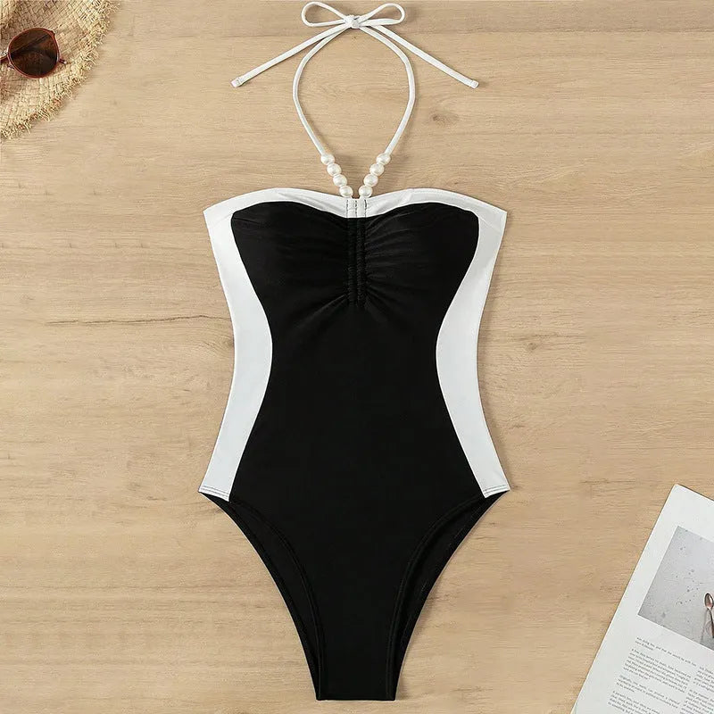 Black and white women's one-piece swimsuit with pearl spaghetti straps, shown on a model.