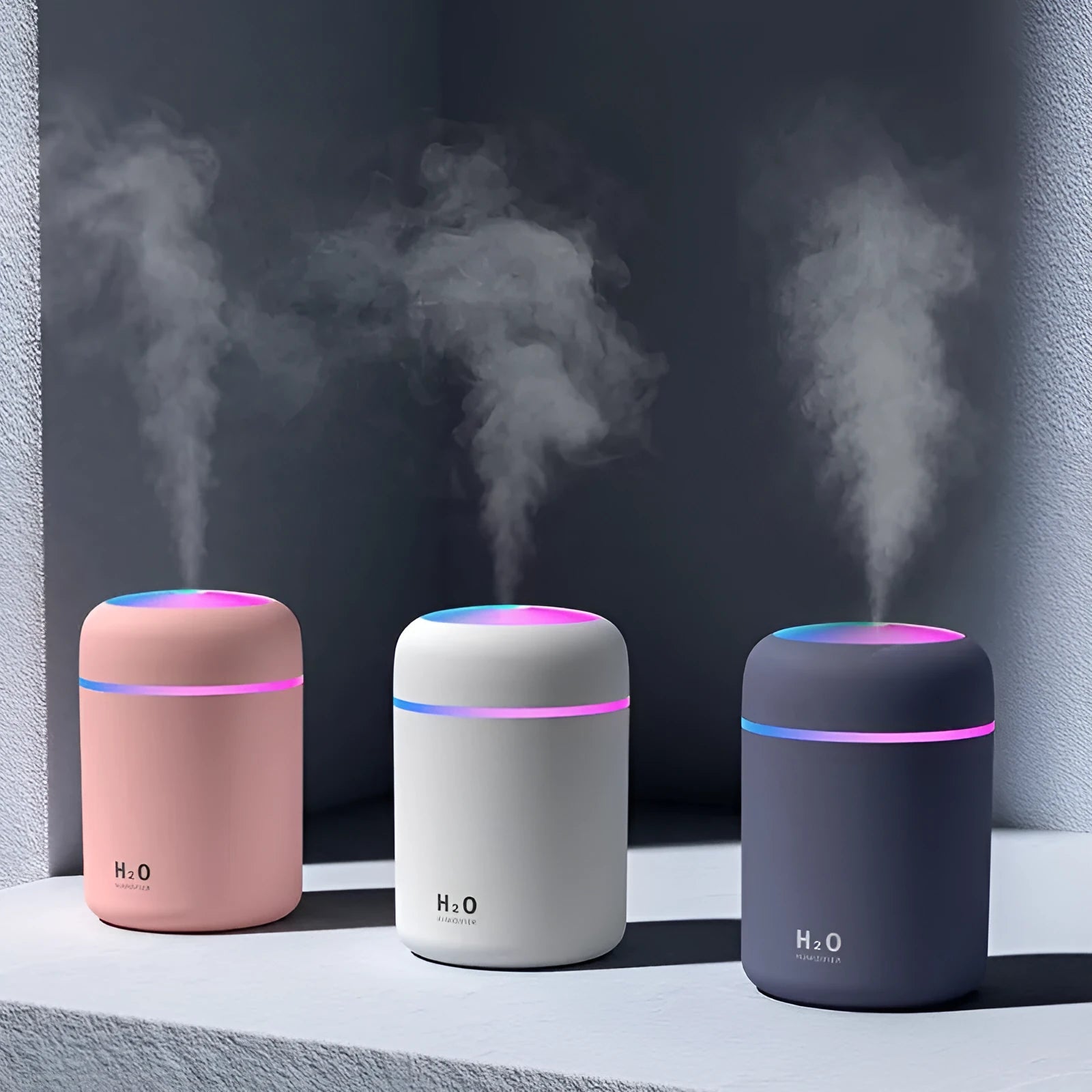 Pink USB desktop humidifier with LED lights and water tank on a wooden desk.