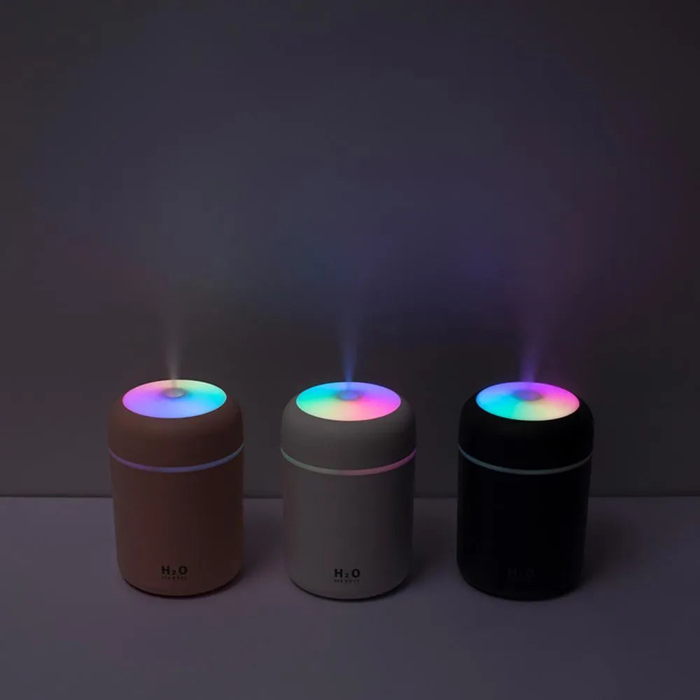 Pink USB desktop humidifier with LED lights and water tank on a wooden desk.