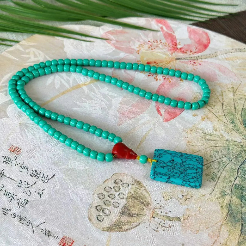 Turquoise lucky pendant necklace with hand-woven mesh flower design on a ball bead chain.