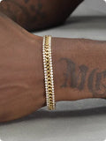 Gold coloured hip hop style tennis bracelet with stone inlay on a wrist.