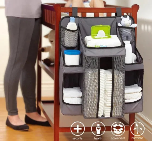 Gray baby diaper organizer hanging on a crib rail with compartments for nappies and wipes