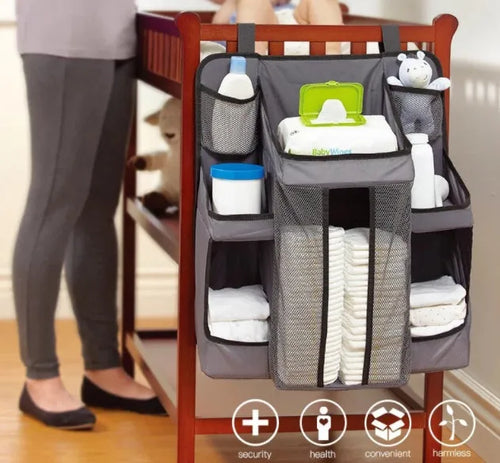 Gray baby diaper organizer hanging on a crib rail with compartments for nappies and wipes