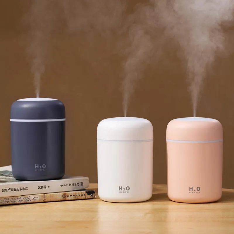 Pink USB desktop humidifier with LED lights and water tank on a wooden desk.