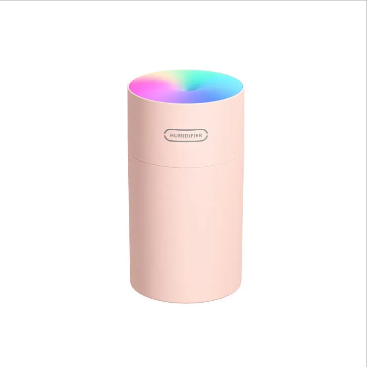 Pink USB desktop humidifier with LED lights and water tank on a wooden desk.