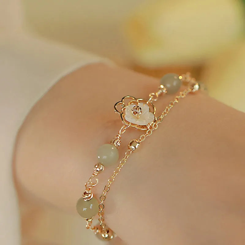 Yellow gold electroplated copper bracelet with a bells of Ireland butterfly, shell flowers, and Hetian jade accents.