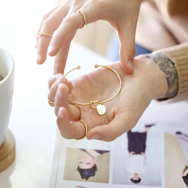 Personalised initial heart knot bracelet in gold finish with custom letter on a white background