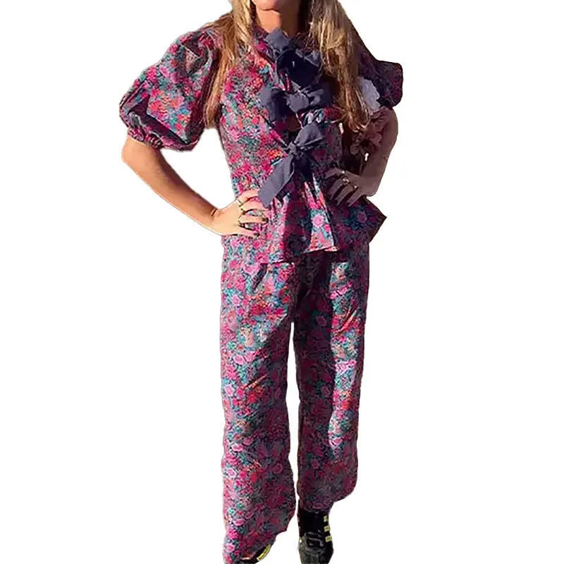 Women's floral print trousers suit with tie-neck puff sleeve top and matching trousers.