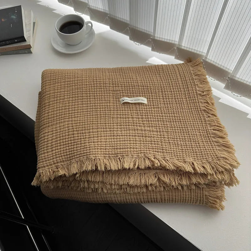 Cotton four-layer gauze blanket with tassel trim in various colours draped over a sofa.